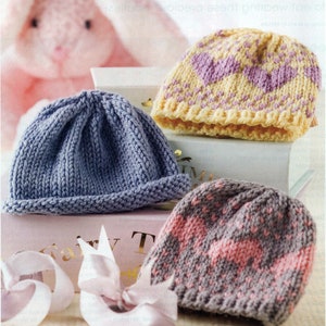 May include: Three knitted baby hats in different colors and patterns. A blue hat, a yellow hat with purple hearts, and a gray hat with pink hearts.