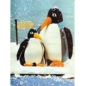 Puede incluir: Dos figuras de pingüinos con cabezas negras, cuerpos blancos y picos y patas naranjas se encuentran en una escena nevada. Un letrero dice "South Pole". El fondo es de color azul claro con motas blancas.