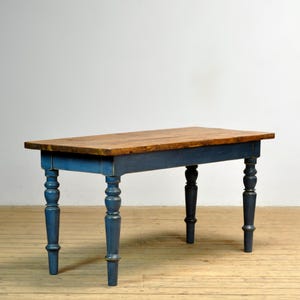 Pode incluir: Uma mesa retangular de madeira com um tampo de madeira natural e uma base pintada de azul. A mesa tem quatro pernas torneadas. As dimensões da mesa são aproximadamente 152 cm de comprimento, 76 cm de largura e 76 cm de altura. Adequada para refeições ou trabalho.