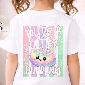May include: White t-shirt featuring a colourful graphic of a smiling dumpling and the text "You're a Glitter Dumpling". The design includes pastel stripes and stars. The shirt is worn by a child.