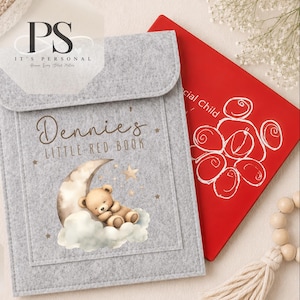 May include: A grey felt envelope-style folder featuring the printed text "Dennie's LITTLE RED BOOK" and an illustration of a teddy bear sleeping on a crescent moon with clouds and stars. A red book with white line art is partially visible behind it.