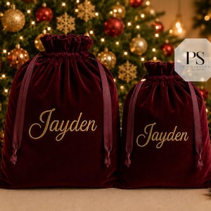 May include: Two deep burgundy velvet drawstring gift bags with ruffled tops and matching ribbon closures. Each bag features the name Jayden embroidered in gold cursive script on the front. The bags are positioned side by side.