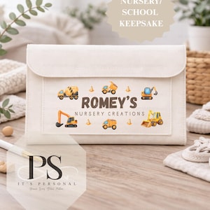 May include: Cream-coloured nursery keepsake bag with a flap. It displays colourful illustrations of construction vehicles and the text "Romey's Nursery Creations." The top of the bag has the text "Nursery/ School Keepsake."