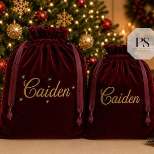 May include: Two deep red velvet drawstring bags with a soft, plush texture. Each bag features the name Caiden printed in a gold script font on the front. The larger bag includes small gold star accents around the name, and both bags have matching red ribbon ties at the top.