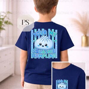 May include: A navy blue t-shirt with a cartoon dumpling design and the text "Your My Squashie Dumpling". The design includes blue stars and vertical stripes. The shirt is worn by a child.