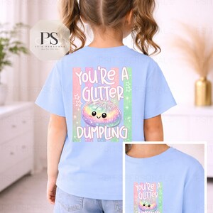 May include: Pale blue t-shirt featuring the words "You're a Glitter Dumpling" and a colourful dumpling illustration. The design includes pastel shades and stars. The shirt is worn by a child.