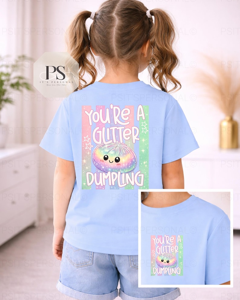May include: Pale blue t-shirt featuring the words "You're a Glitter Dumpling" and a colourful dumpling illustration. The design includes pastel shades and stars. The shirt is worn by a child.