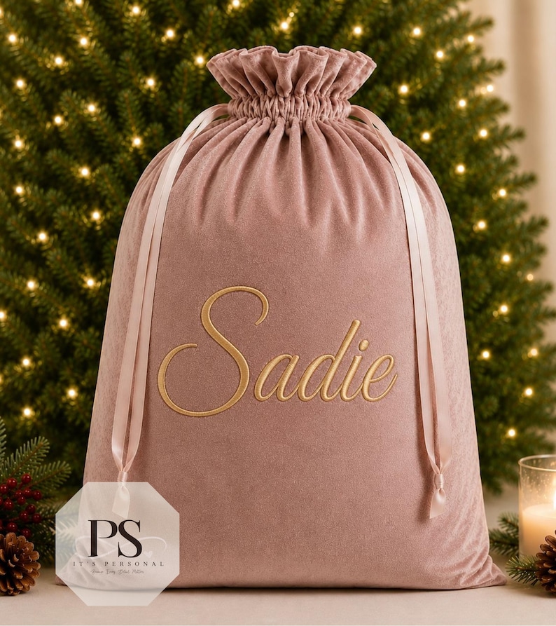 May include: A dusty rose velvet drawstring gift bag featuring the name Sadie embroidered in gold script lettering on the front. The bag has a ruffled top edge and matching satin ribbon ties that cinch the opening closed for secure storage.