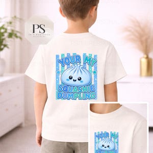May include: White t-shirt featuring a blue and turquoise dumpling graphic with the words "YOUR MY SQUASHIE DUMPLING". The design includes stars and a striped background. A smaller version of the design is also visible.