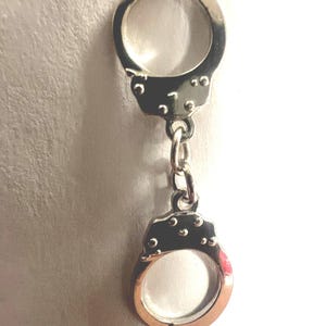 May include: Silver-toned metal handcuffs charm with a linked chain. The charm is a miniature replica of a pair of handcuffs.