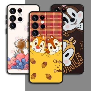 May include: Three phone cases featuring Chip and Dale from Disney's Chip 'n Dale Rescue Rangers. The first case is white with a pink and purple fruit design. The second case is yellow with a plaid design and the text "Chip 'n Dale". The third case is brown with a black and white design.