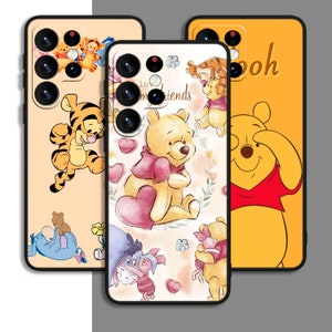 May include: Three phone cases featuring Winnie the Pooh and his friends. The first case is yellow with a cartoon image of Winnie the Pooh covering his eyes. The second case is white with a cartoon image of Winnie the Pooh holding a heart. The third case is peach with a cartoon image of Tigger jumping. All three cases have black borders.