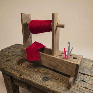 Può includere: Un rocchetto di legno con una bobina di filo rosso e un piccolo pezzo di tessuto a maglia rosso. Il rocchetto tiene il filo, e il tessuto viene lavorato con un uncinetto. Il testo "BROWN colour" è in basso.