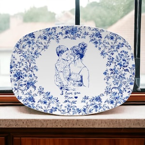 May include: Oval serving platter with a blue and white floral design. The center features a blue sketch of a mother and child with the text "I love you Mom". The platter is made of ceramic.