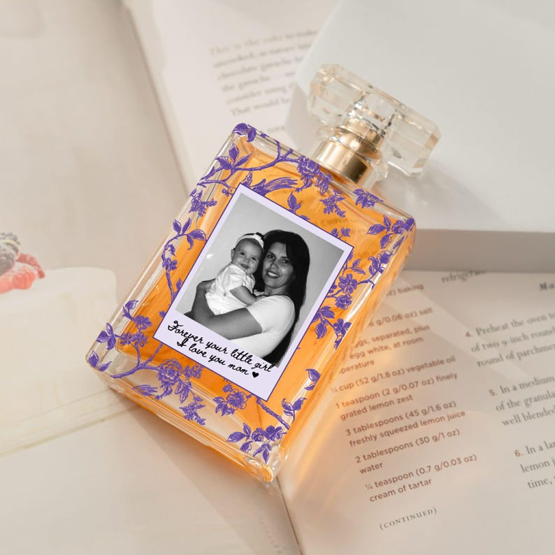 May include: A clear perfume bottle with a gold cap and a photo of a mother and child. The bottle has a floral design in purple and the text "Forever your little girl, I love you mom."