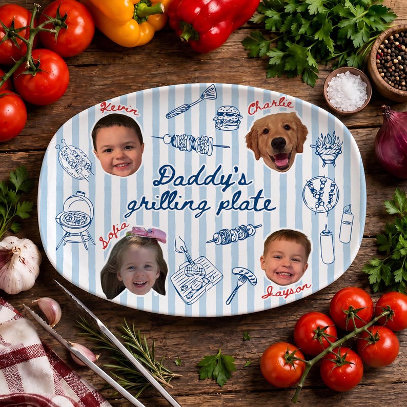 May include: An oval ceramic serving plate with a light blue and white striped pattern. The text "Daddy's grilling plate" is centered, surrounded by blue line drawings of grilling tools and food, plus four circular portraits of children and a dog.