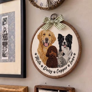 May include: A circular embroidery hoop wall hanging featuring a stitched portrait of three dogs and one cat. The names Milo, Daisy, Cupper, and Luna are embroidered in black script below the animals, accented by a green and white gingham bow.