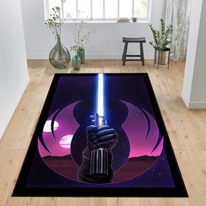 Puede incluir: Una alfombra negra y morada con un dise&ntilde;o de tem&aacute;tica de Star Wars. La alfombra presenta un sable de luz con una hoja azul y un s&iacute;mbolo de la Alianza Rebelde.