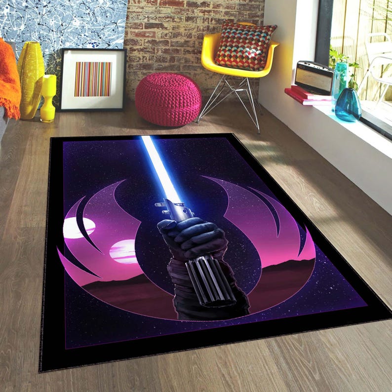 Puede incluir: Una alfombra negra y morada con un s&iacute;mbolo de la Alianza Rebelde de Star Wars y un sable de luz. El sable de luz es azul y tiene un mango negro. El s&iacute;mbolo est&aacute; rodeado de estrellas.