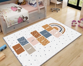 Puede incluir: Una alfombra de juego blanca con un diseño de hopscotch con los números del 1 al 8. La alfombra tiene un arcoíris y lunares blancos.