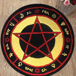Puede incluir: Una alfombra redonda negra y roja con un centro amarillo y una estrella roja de cinco puntas. La alfombra tiene un borde negro con letras rojas que dicen "AL PHA OME GY", "DIT", "HA", "NU", "IT" y "Q".
