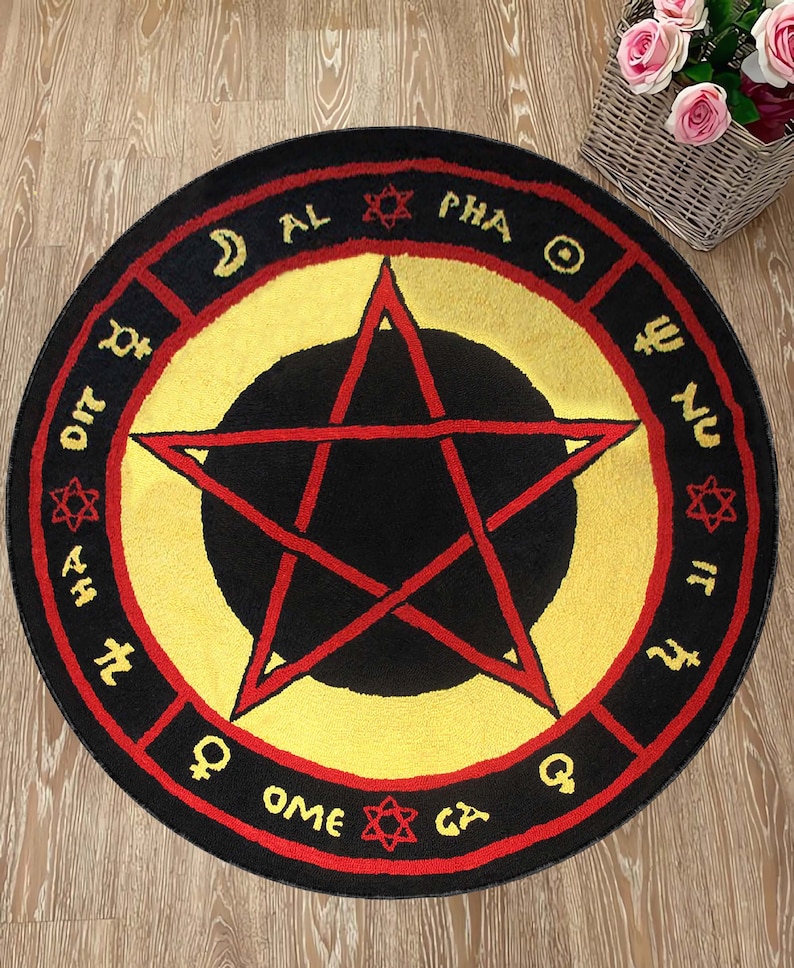 Puede incluir: Una alfombra redonda negra y roja con un centro amarillo y una estrella roja de cinco puntas. La alfombra tiene un borde negro con letras rojas que dicen "AL PHA OME GY", "DIT", "HA", "NU", "IT" y "Q".