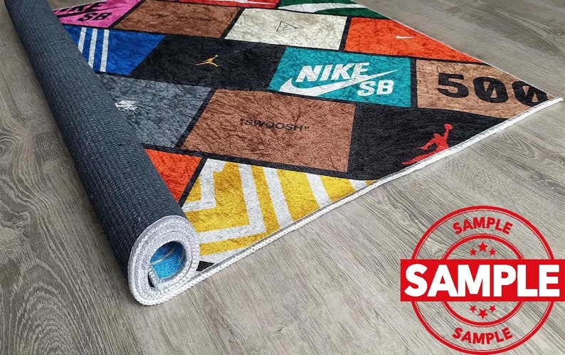 Puede incluir: Una alfombra colorida con un patr&oacute;n geom&eacute;trico que presenta varios logotipos de marcas, incluyendo Nike, SB y 500. La alfombra tiene un borde blanco y est&aacute; enrollada.