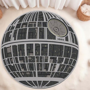 May include: A round, grey and black area rug with a design that resembles the Death Star from Star Wars. The rug has a black centre with a small, grey circle in the middle.