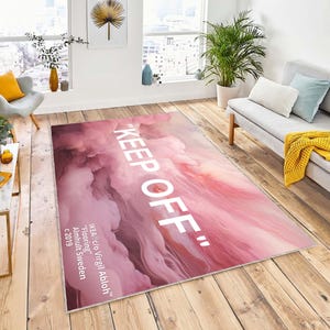 May include: A pink and white rug with the text "KEEP OFF" in white lettering. The rug has a marbled, cloudy design. The text "IKEA c/o Virgil Abloh™" is in the bottom left corner, along with "Flooring", "Almhult Sweden", and "c 2019".