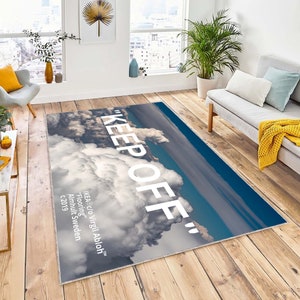 Può includere: Un tappeto bianco con un design di cielo blu e nuvole bianche. Il testo "KEEP OFF" è stampato in grandi lettere bianche su tutto il tappeto. Il testo "IKEA c/o Virgil Abloh™" è stampato in lettere bianche più piccole nell'angolo in basso a destra del tappeto.