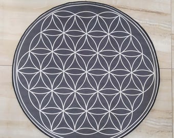 Op de afbeelding: Een ronde, donkergrijze vloerkleed met een wit geometrisch bloem des levens patroon. Het vloerkleed heeft een zwarte rand en een witte buitenring. Het symmetrische ontwerp bedekt het gehele oppervlak van het vloerkleed. Diameter ca. 120 cm.