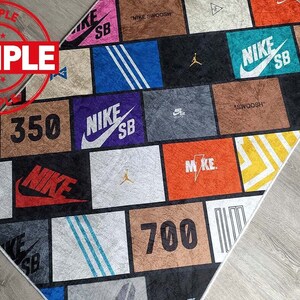 Puede incluir: Una alfombra colorida con un dise&ntilde;o de patchwork que presenta varios logotipos de Nike, incluido el swoosh de Nike, las palabras "Nike SB" y los n&uacute;meros "350", "500" y "700".