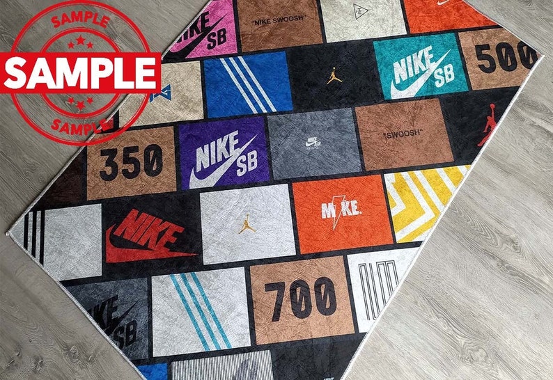 Puede incluir: Una alfombra colorida con un dise&ntilde;o de patchwork que presenta varios logotipos de Nike, incluido el swoosh de Nike, las palabras "Nike SB" y los n&uacute;meros "350", "500" y "700".