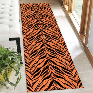 May include: Orange and black tiger stripe patterned rug. The rug has a long, narrow shape and is ideal for a hallway or entryway.