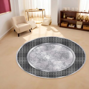 May include: A round, silver and black area rug with a distressed metal design. The rug has a circular pattern around the edge and a large, oval-shaped center.