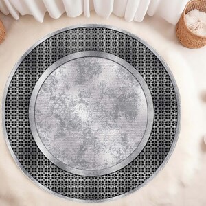 May include: A round, silver and black area rug with a geometric pattern. The rug has a large, circular, silver center with a distressed, metallic look.