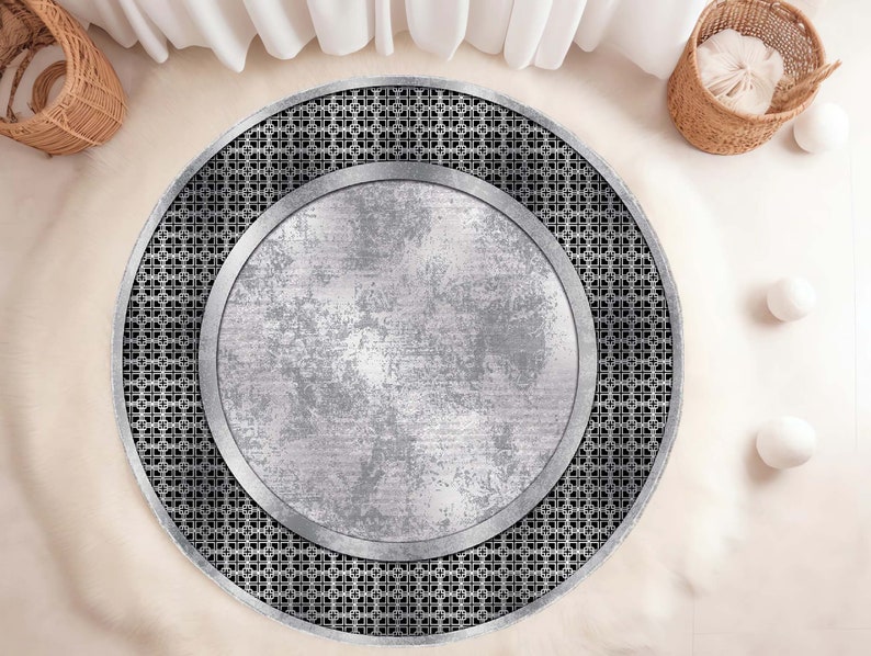 May include: A round, silver and black area rug with a geometric pattern. The rug has a large, circular, silver center with a distressed, metallic look.