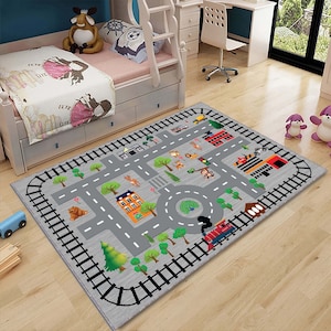 May include: A gray play mat with a city street design. The mat features a train track border, a roundabout, buildings, trees, animals, and traffic lights.