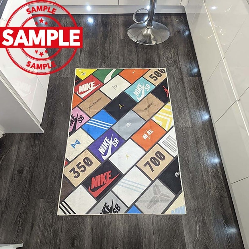 Puede incluir: Una alfombra colorida con un patr&oacute;n geom&eacute;trico que presenta el logotipo de Nike y los n&uacute;meros 350, 500 y 700. La alfombra est&aacute; hecha de un material suave y duradero y es perfecta para agregar un toque de estilo a cualquier habitaci&oacute;n.