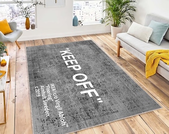 Könnte beinhalten: Ein grauer und weißer Teppich mit dem Text "KEEP OFF" in weißen Buchstaben. Der Teppich hat einen abgenutzten, Vintage-Look und enthält den Text "IKEA c/o Virgil Abloh" und "Flooring" in kleineren weißen Buchstaben.