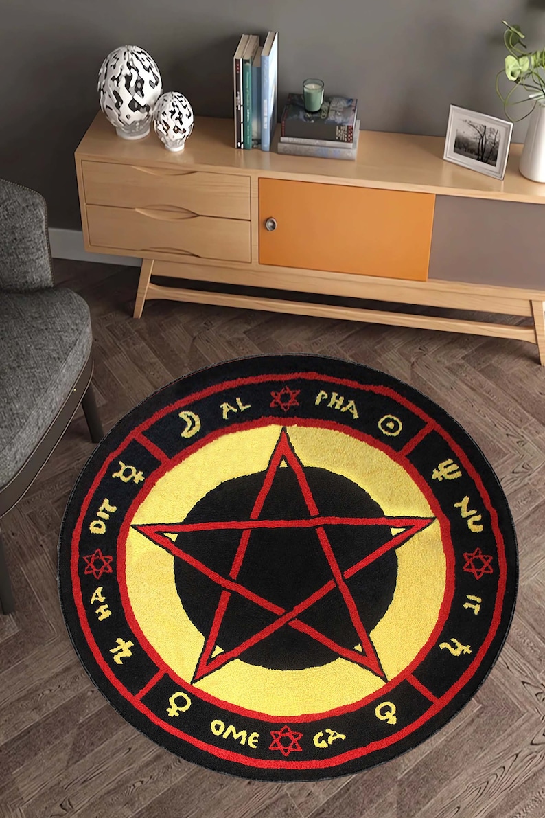 Puede incluir: Una alfombra redonda negra y amarilla con un pentagrama rojo en el centro. La alfombra tiene un borde rojo con texto negro alrededor del borde. El texto incluye las palabras "AL", "PHA", "OME" y "GA".