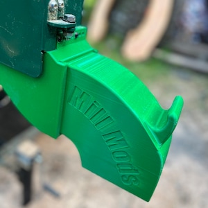 May include: A green plastic dust collection attachment for a woodworking machine. The attachment has the words "Mill Mods" printed on it.