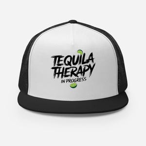 May include: A black and white trucker hat with a white front panel and a black mesh back. The front panel features the text "Tequila Therapy In Progress" in black with a lime wedge graphic.