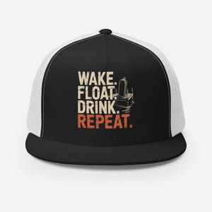 Op de afbeelding: Zwart-witte truckercap met een wit mesh achterpaneel. De cap heeft een afbeelding van een dok met een koelbox en de tekst "WAKE. FLOAT. DRINK. REPEAT."