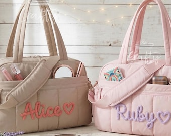 Puede incluir: Dos bolsos tote acolchados, uno beige y otro rosa, con correas para el hombro y bolsillos exteriores. El bolso beige tiene "Alice" bordado en coral, y el bolso rosa tiene "Ruby" bordado en lavanda. Ambos bolsos contienen maquillaje y accesorios.