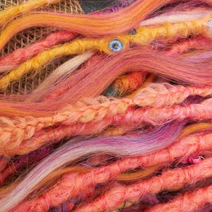 May include: A close-up of a variety of colorful synthetic dreadlocks. The dreadlocks are made of a variety of colors, including pink, orange, yellow, and purple. The dreadlocks are arranged in a loose, flowing pattern.