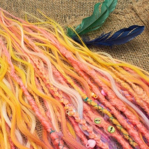 May include: A collection of colorful synthetic dreadlocks in shades of pink, yellow, and white. The dreadlocks are decorated with beads and are arranged on a burlap background.