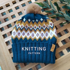May include: A teal knitted hat with a brown pom-pom and a geometric pattern in white, gold, and maroon. The hat has a ribbed brim and a small tag. The text "KNITTING PATTERN" is displayed on the hat.