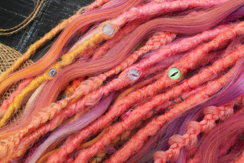 May include: A close-up of a set of colorful synthetic dreadlocks with beads. The dreadlocks are a mix of pink, orange, and purple.