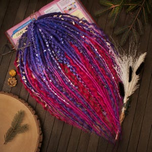 May include: A set of synthetic dreadlocks featuring a vibrant gradient of deep purple, blue, and bright magenta. The strands are a mix of straight and wavy textures, accented with silver-toned charms, beads, and thin decorative wrapping threads.